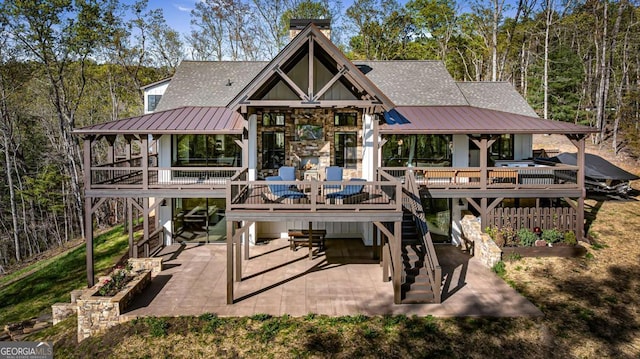 rear view of property with a wooden deck, a shingled roof, metal roof, and a patio