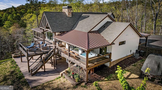 back of property featuring a standing seam roof, a shingled roof, a view of trees, and a deck