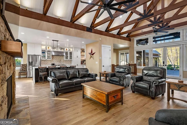 living room with a healthy amount of sunlight, a ceiling fan, beamed ceiling, light wood-style floors, and high vaulted ceiling