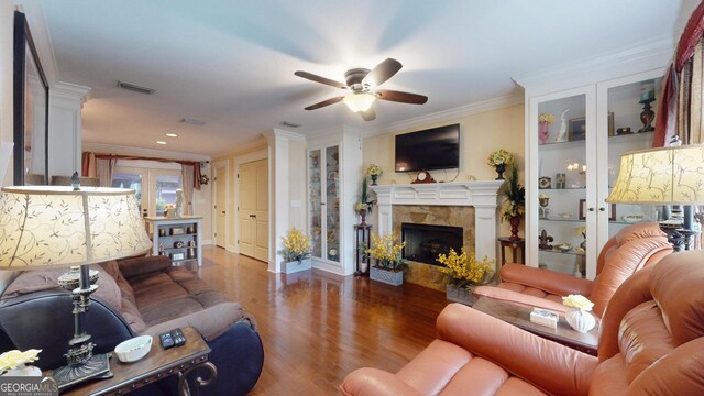 living area featuring visible vents, wood finished floors, ceiling fan, crown molding, and a fireplace