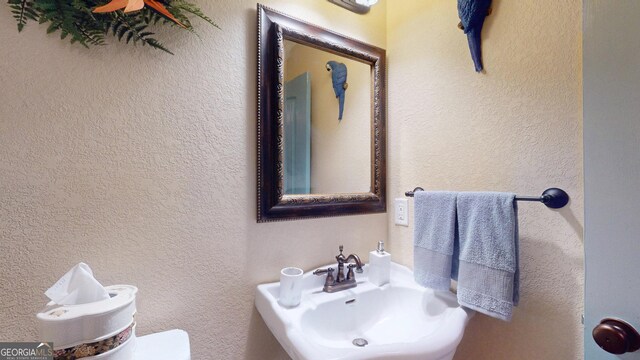 half bath featuring a textured wall, toilet, and a sink