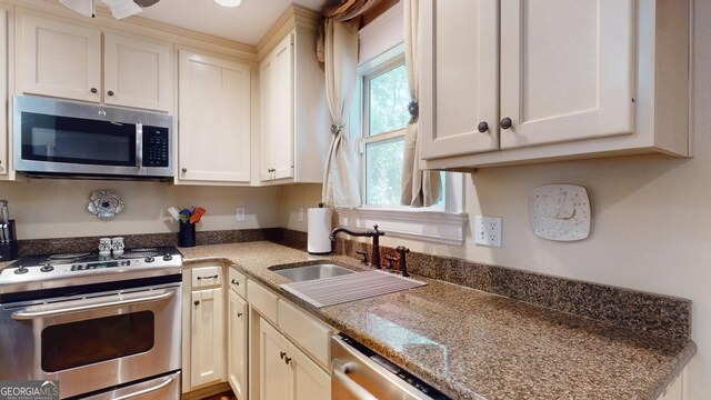 kitchen with stainless steel appliances, a sink, white cabinetry, and dark stone counters
