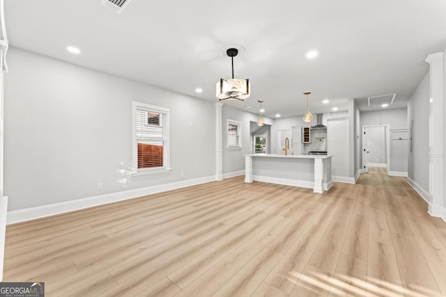 unfurnished living room featuring recessed lighting, a sink, baseboards, attic access, and light wood-style flooring