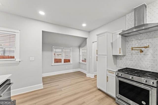 kitchen with light wood-type flooring, white cabinetry, wall chimney range hood, light countertops, and appliances with stainless steel finishes