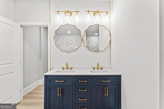bathroom featuring baseboards, wood finished floors, a sink, and double vanity