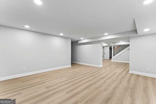 finished below grade area with light wood-style flooring, baseboards, recessed lighting, and stairs