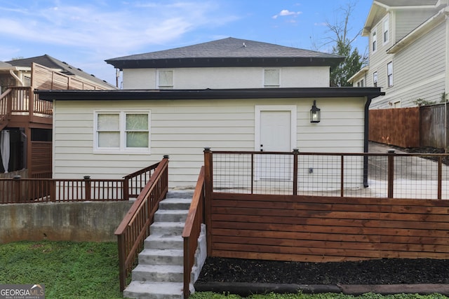 back of property with stairway, fence, and roof with shingles