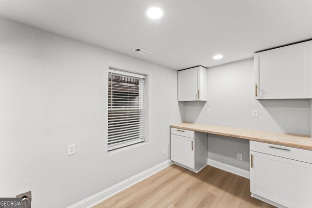 unfurnished office featuring built in desk, light wood-type flooring, baseboards, visible vents, and recessed lighting