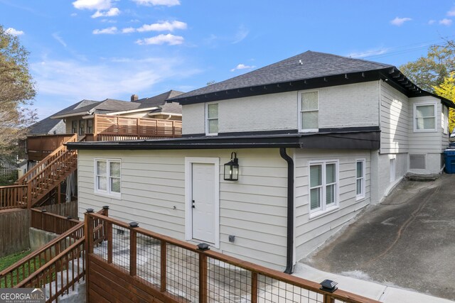 back of house with roof with shingles, stairway, and fence