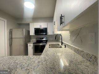 kitchen featuring a sink, freestanding refrigerator, light stone countertops, black microwave, and electric stove