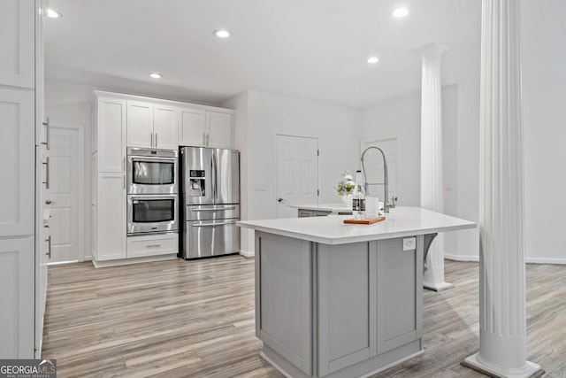 515 Old Chartwell Xing, Alpharetta, GA 30022 - kitchen featuring appliances with stainless steel finishes, a sink, light wood-style floors, light countertops, and an island with sink
