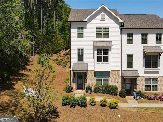 multi unit property with brick siding, a shingled roof, a standing seam roof, and metal roof