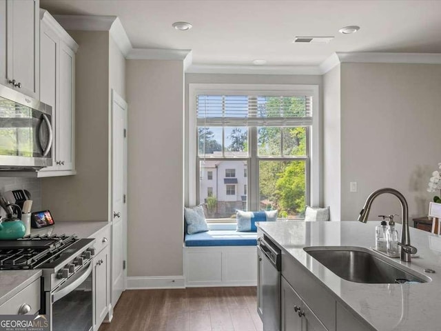 kitchen featuring a sink, appliances with stainless steel finishes, ornamental molding, light stone countertops, and dark wood-type flooring