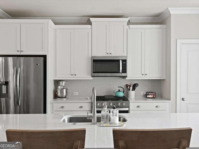 kitchen with white cabinets, light stone counters, stainless steel appliances, a sink, and tasteful backsplash
