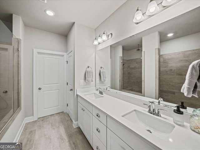 full bathroom with baseboards, a sink, double vanity, and tiled shower