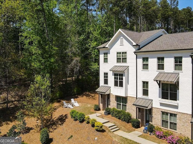 view of side of property featuring a standing seam roof, brick siding, and roof with shingles