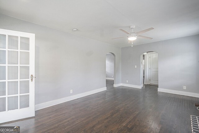 unfurnished room featuring arched walkways, dark wood finished floors, baseboards, and ceiling fan
