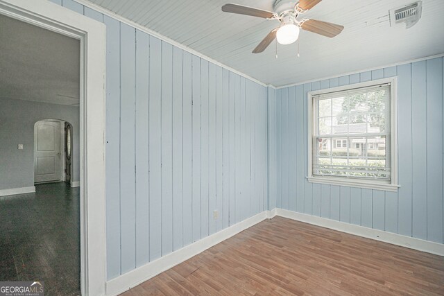 unfurnished room featuring arched walkways, wood finished floors, visible vents, and baseboards