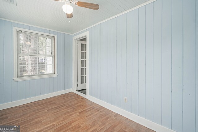 empty room featuring baseboards, wood finished floors, ceiling fan, crown molding, and wooden walls