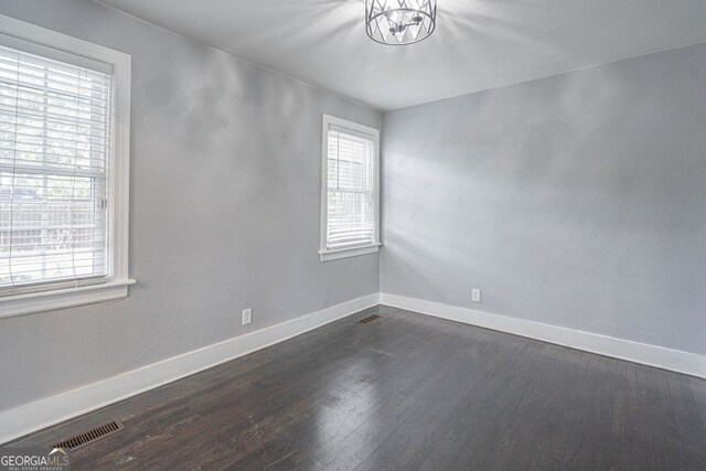 spare room with baseboards, visible vents, a notable chandelier, and dark wood finished floors