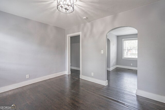 spare room with arched walkways, dark wood finished floors, a chandelier, and baseboards