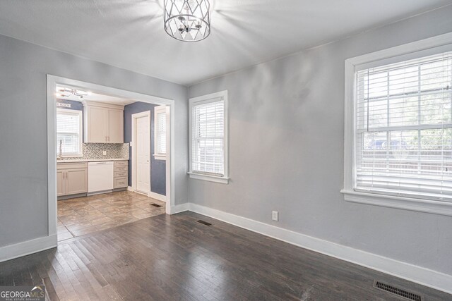 unfurnished dining area with baseboards, visible vents, an inviting chandelier, and dark wood-style floors