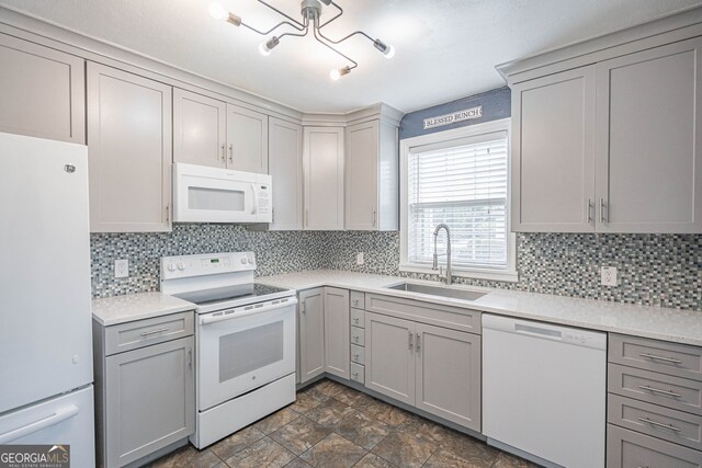 kitchen featuring tasteful backsplash, gray cabinetry, a sink, and white appliances