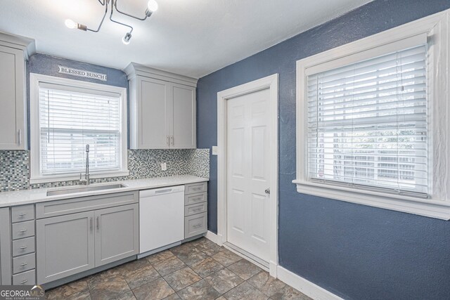 kitchen featuring tasteful backsplash, dishwasher, baseboards, and a sink