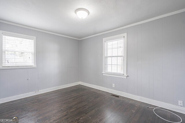empty room with dark wood-style floors, baseboards, crown molding, and visible vents
