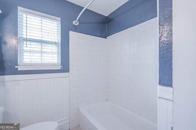 bathroom with tub / shower combination, toilet, and wainscoting