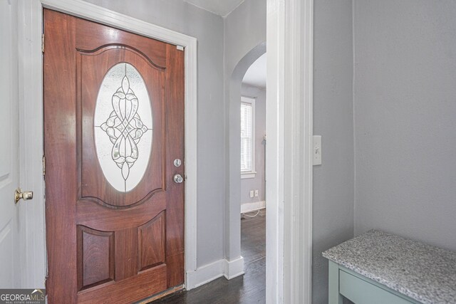 foyer with arched walkways, dark wood finished floors, and baseboards