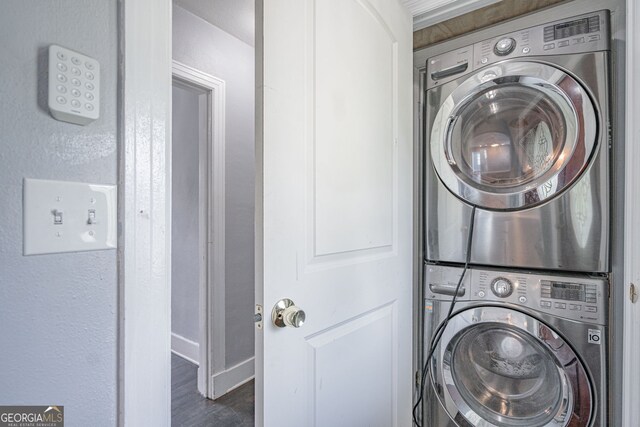 clothes washing area featuring baseboards, wood finished floors, stacked washing maching and dryer, and laundry area