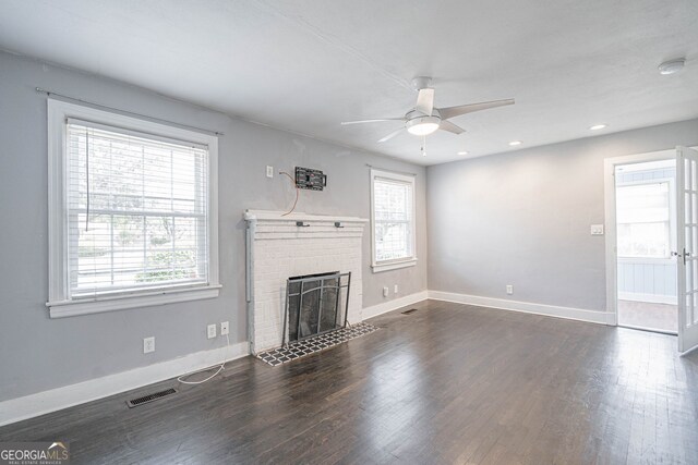 unfurnished living room featuring ceiling fan, a fireplace, baseboards, dark wood-style flooring, and visible vents
