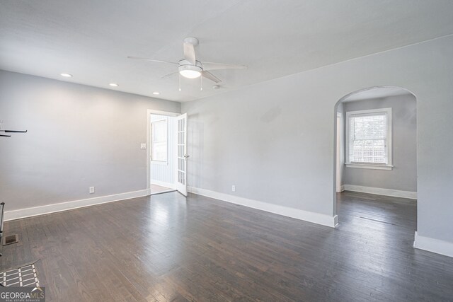 unfurnished room featuring arched walkways, a ceiling fan, dark wood-style floors, and baseboards