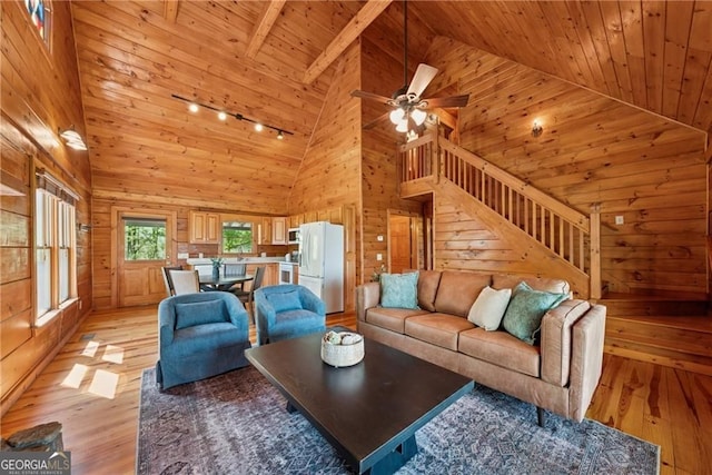 living area with light wood-type flooring, wood walls, stairway, track lighting, and high vaulted ceiling