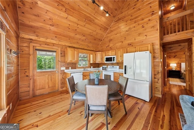 dining space with rail lighting, wood walls, lofted ceiling, and light wood-style flooring