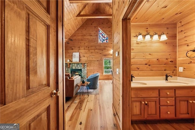 bathroom featuring wooden walls, hardwood / wood-style floors, wooden ceiling, and a sink