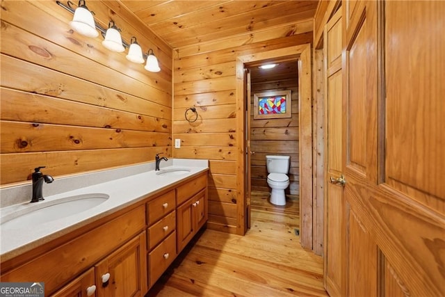 full bath featuring wooden walls, wood finished floors, a sink, and toilet