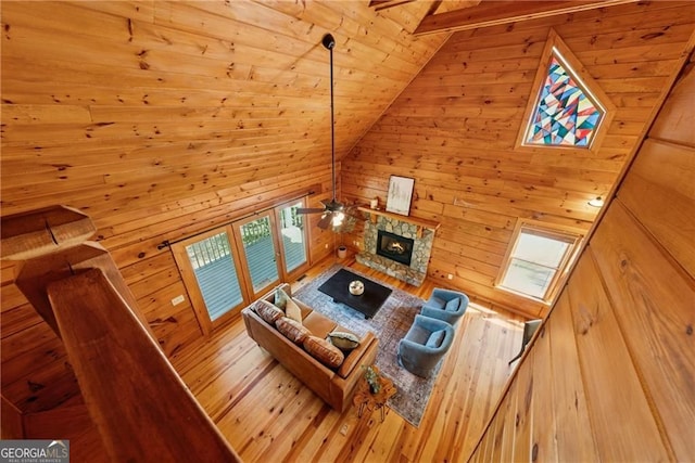 living area featuring lofted ceiling, wood walls, a stone fireplace, a ceiling fan, and wooden ceiling