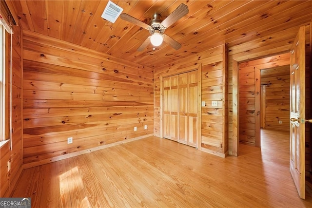 unfurnished room featuring wooden walls, visible vents, a ceiling fan, wooden ceiling, and light wood-style flooring