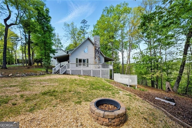 rear view of house featuring a chimney, a wooden deck, an outdoor fire pit, and a lawn