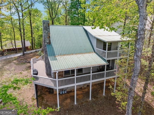 rear view of property with a chimney, a balcony, and metal roof