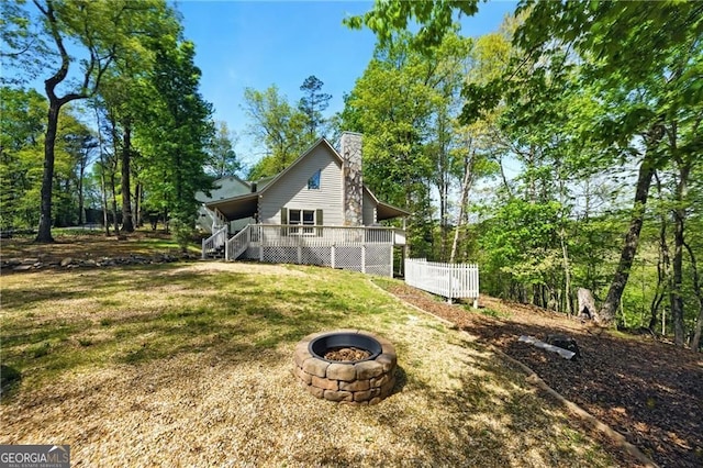 view of home's exterior with a wooden deck, a lawn, a fire pit, and a chimney