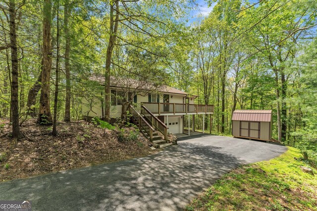 view of front of house with an outdoor structure, aphalt driveway, an attached garage, a storage shed, and stairway