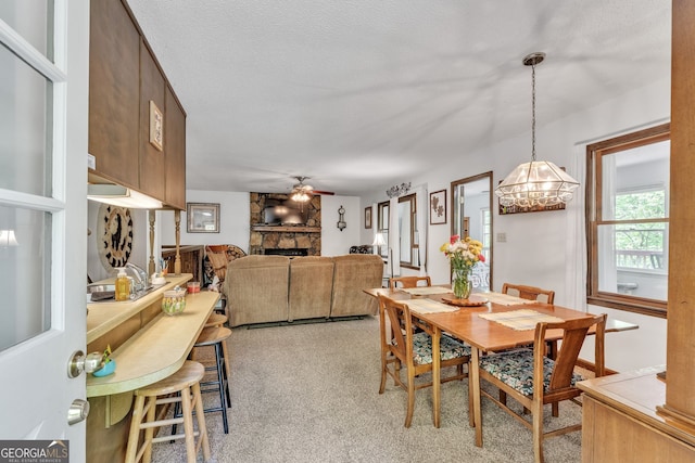 dining area with a stone fireplace, light carpet, and ceiling fan with notable chandelier