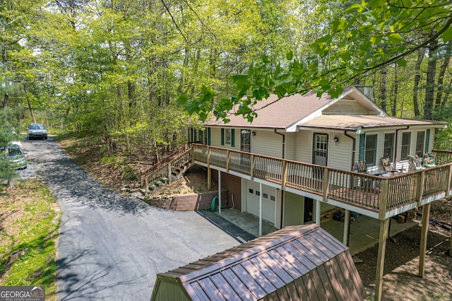 rear view of house with an attached garage, driveway, a wooden deck, and a shingled roof