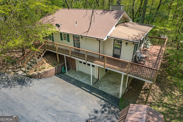 rear view of property featuring a garage, a view of trees, aphalt driveway, and a wooden deck
