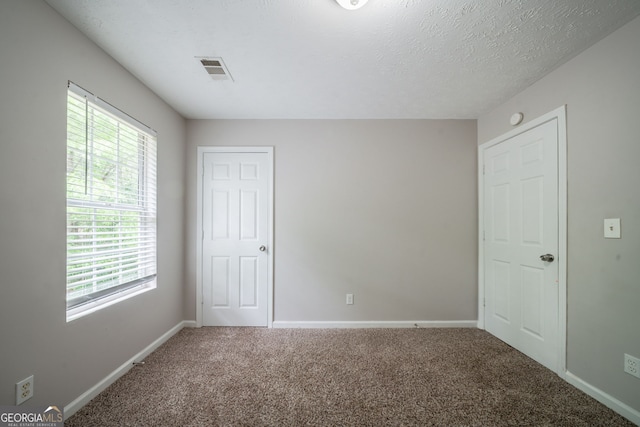spare room featuring carpet floors, visible vents, and a healthy amount of sunlight