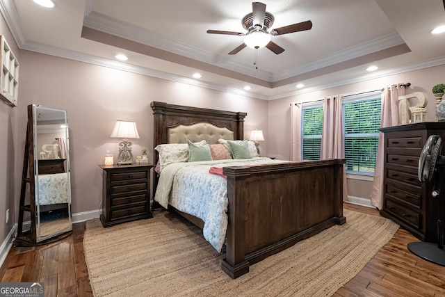 bedroom featuring baseboards, crown molding, a tray ceiling, and hardwood / wood-style flooring