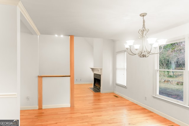 unfurnished dining area featuring a fireplace with flush hearth, an inviting chandelier, light wood-style floors, and baseboards